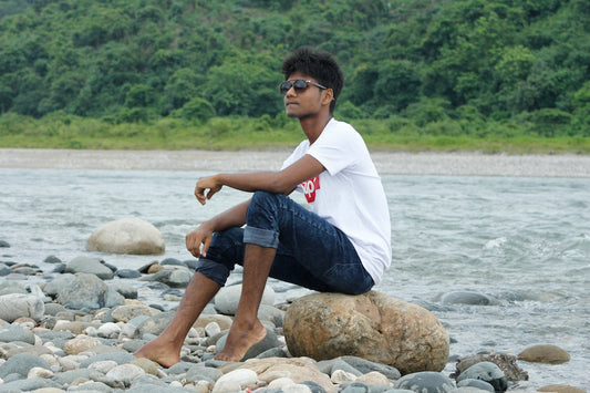man in white shirt and blue denim jeans sitting on rock near river during daytime